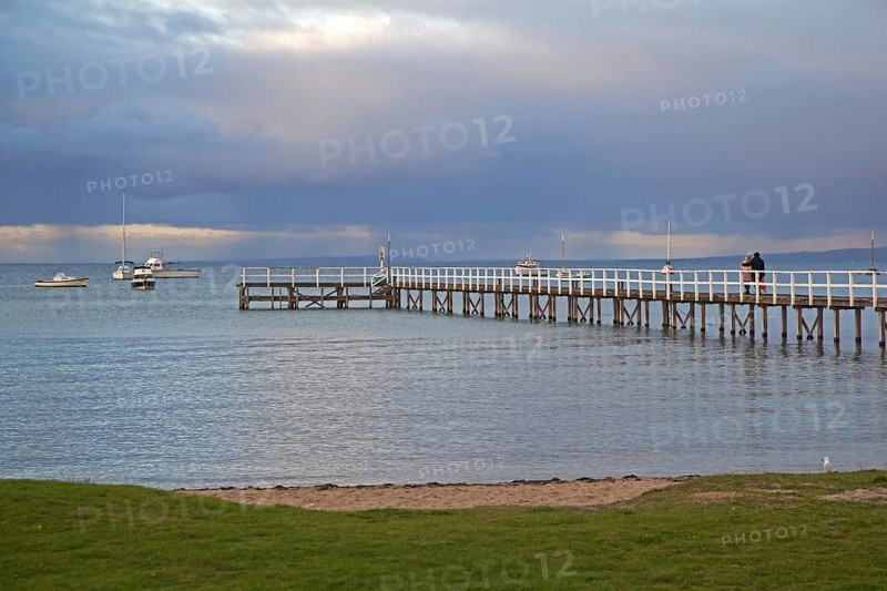 Couple watching sunset from wooden jetty at seaside resort Sorrento in the Port Phillip Bay