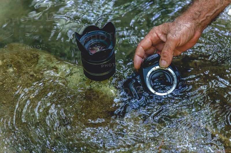 A man cleans the sensor of his reflex camera in the water of a river by flooding it from the inside