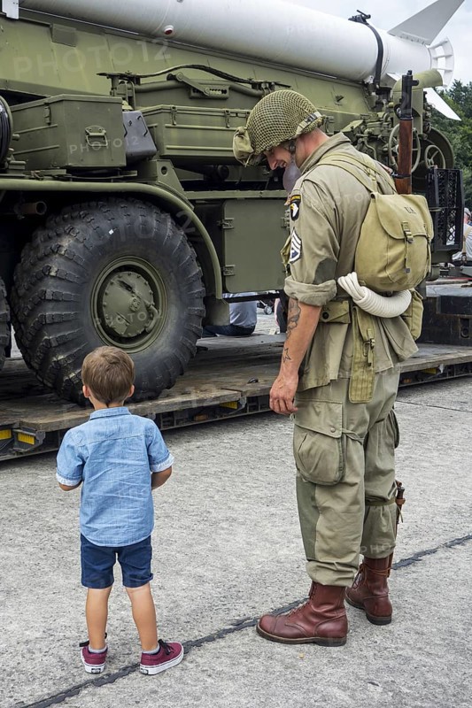 Little boy and WW2 reenactor in US soldier outfit looking at missile truck at World War Two militaria fair