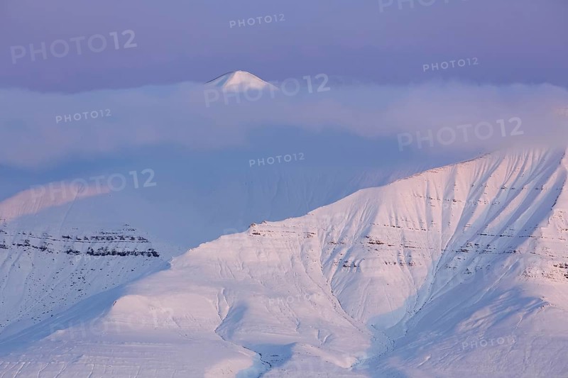 Snow covered mountain peak partially hidden by cloud at sunset at Billefjorden