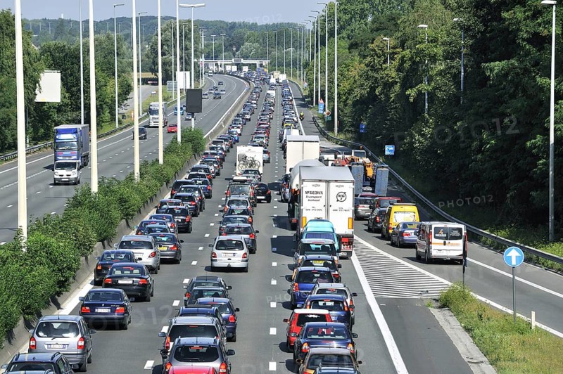 Cars and trucks queueing in highway lanes at approach slip road during traffic jam on motorway during summer holidays