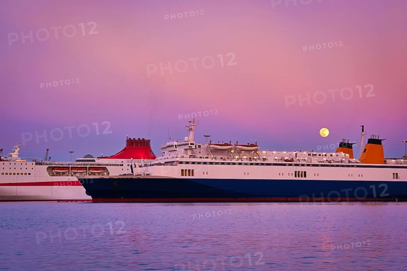 Two ferries moored parallel by pier at colorful sunset during moonrise. Popular transportation for island hopping in Mediterranean sea