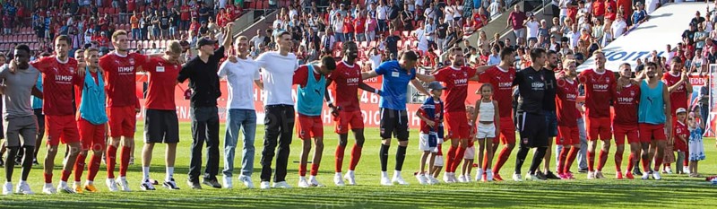 The 1.FC Heidenheim team celebrates the victory under the fan curve