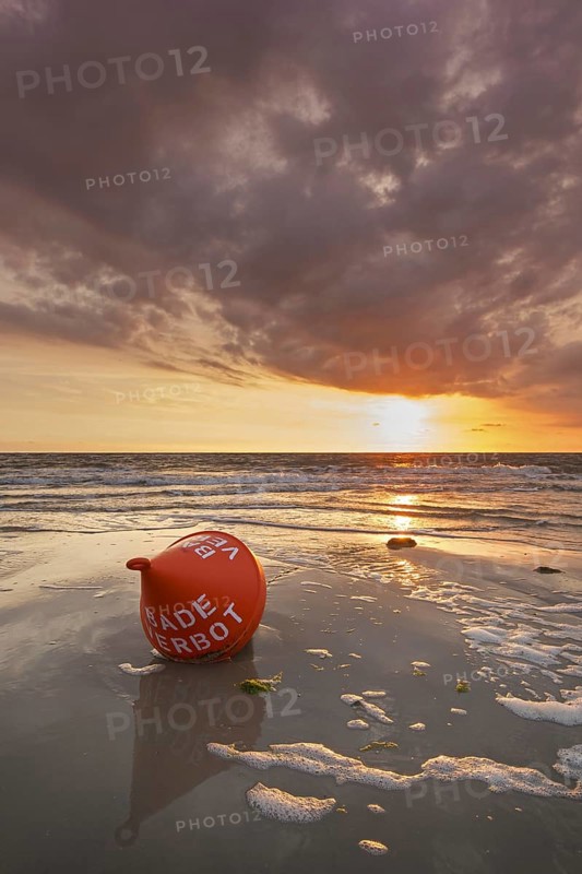 Seascape showing orange buoy on the beach at low tide and sunset over the Wadden Sea