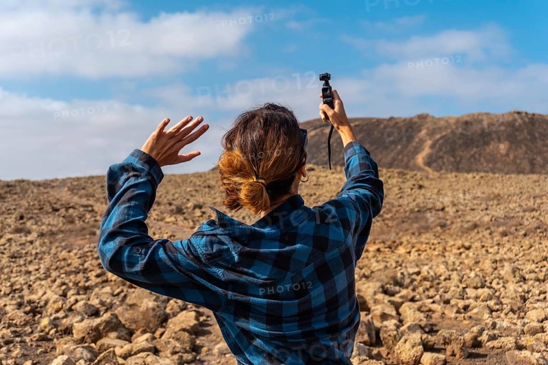 A young woman taking photos with a handheld camera next to the Crater of the Calderon Hondo volcano near Corralejo