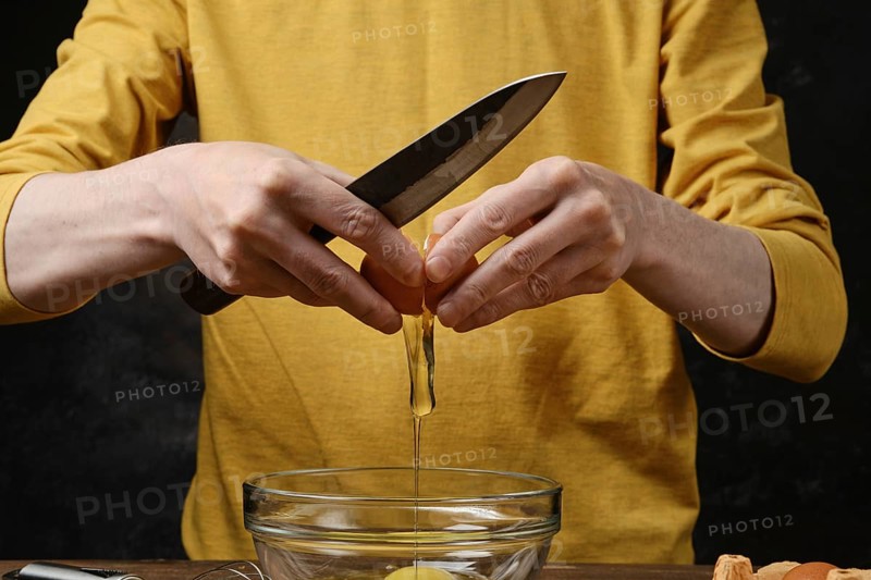Unrecognizable man breaks eggs into a glass bowl to make an omelette