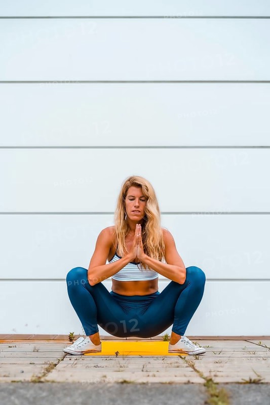 Yoga with blonde caucasian girl doing exercise on a yellow mat with white wall in the background