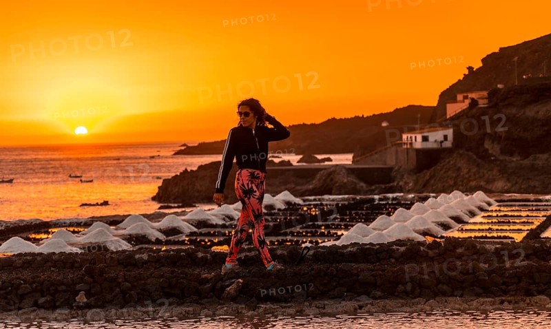 A young woman walking in the orange sunset in the salina and in the background the Fuencaliente Lighthouse on the route of the volcanoes south of the island of La Palma