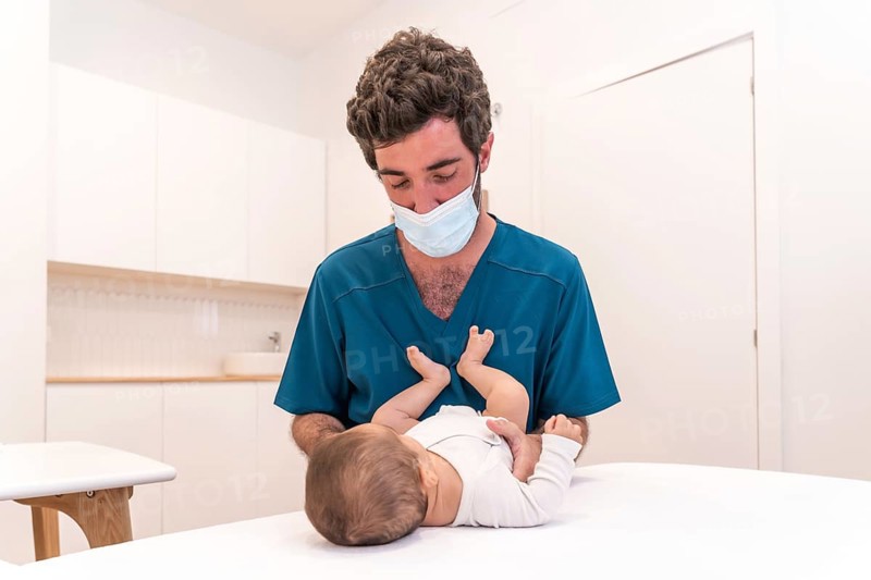 Portrait of a young doctor checking up a baby lying down on stretcher in a clinic