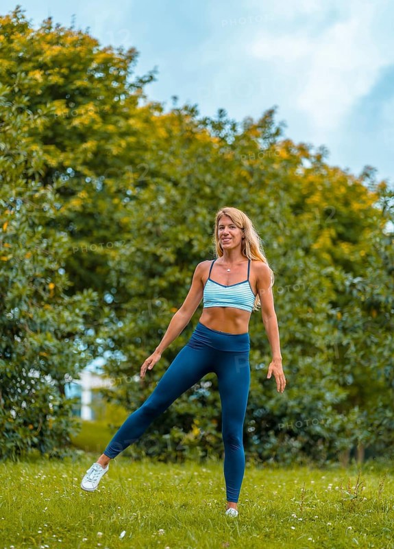 Fitness session with a young blonde Caucasian woman exercising on the street with a blue maya on her feet and a white short shirt. Performing side jumps