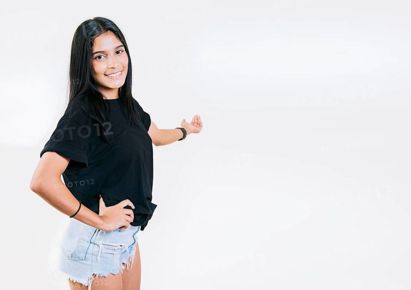 Happy young girl welcoming you isolated. Smiling latin girl pointing back presenting a product. Latin girl pointing a promotion with her palm