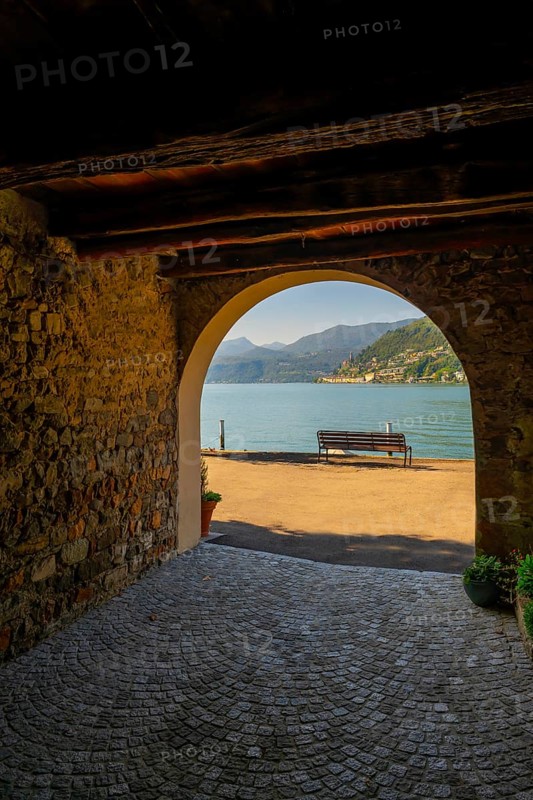 Old Beautiful Street Tunnel with Arch and a Bench from Brusino Arsizio on the Waterfront in a Sunny Summer Day and with Lake Lugano and Mountain View over Morcote