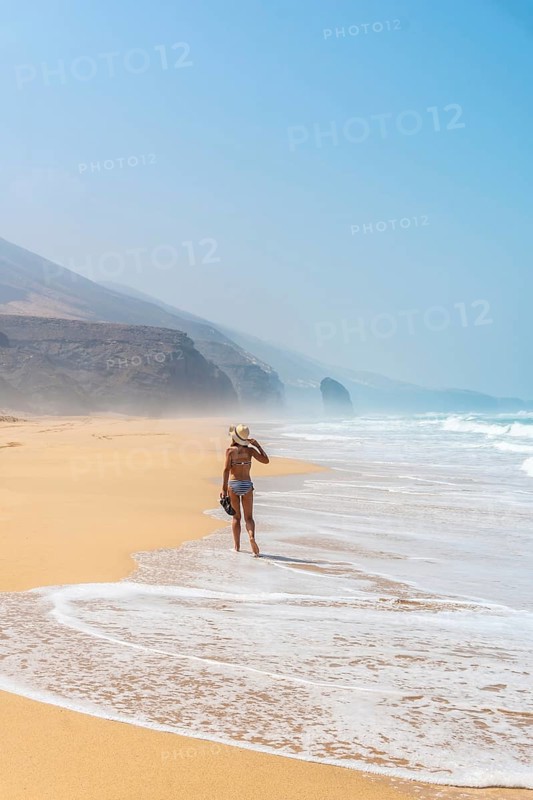 A young tourist with a hat walking alone on the Cofete beach of the Jandia natural park