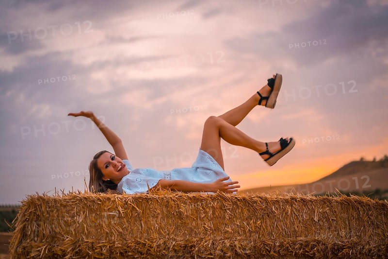 A young blonde Caucasian woman in a white dress in a field of dry straw atop a haystack. In a dry cultivated field in Navarra