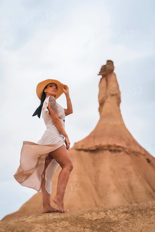 Brunette Caucasian model with a white dress and a straw hat in the Castildetierra of the Bardenas Reales desert