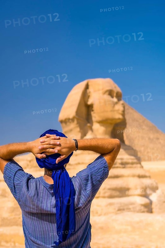 A young tourist enjoying and admiring the Great Sphinx of Giza dressed in blue and a blue turban. Cairo