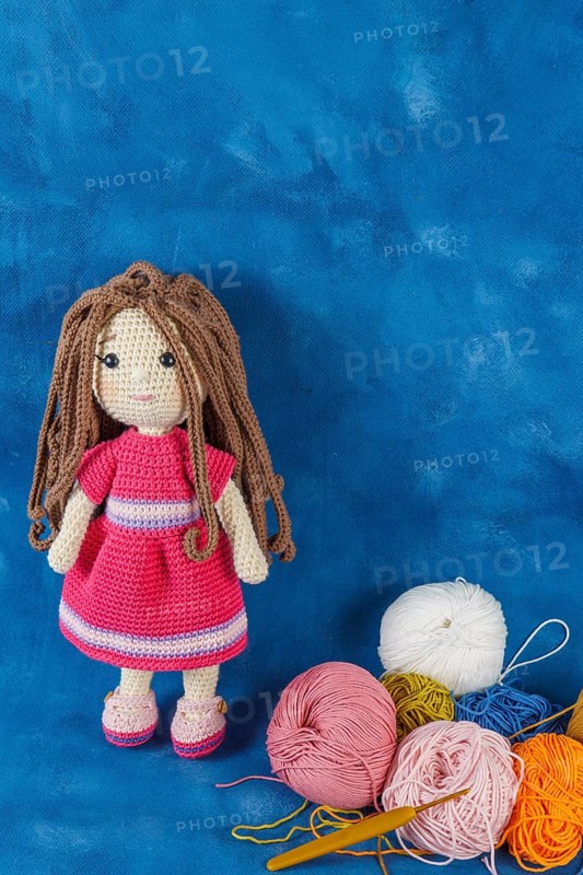 Amigurumi doll handmade on a blue background with the yarns used for its elaboration
