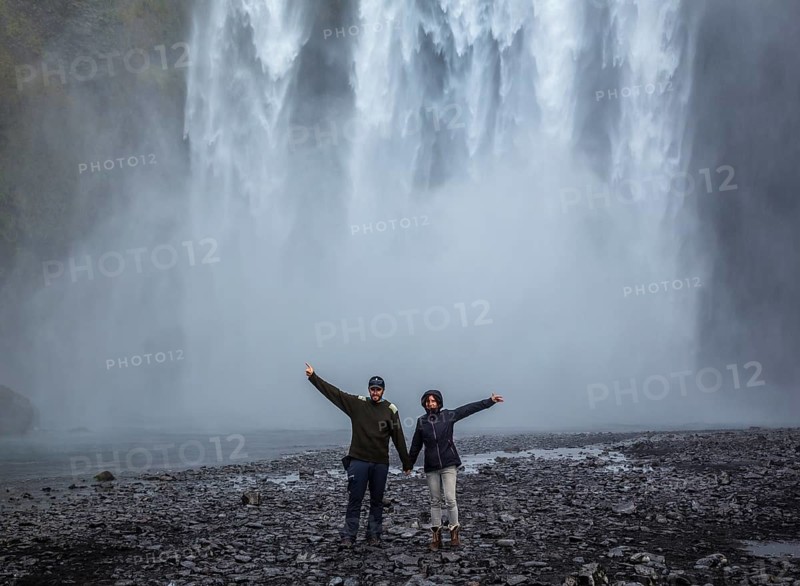 A couple with open arms at the bottom of the Skogafoss waterfall in the golden circle of the south of Iceland