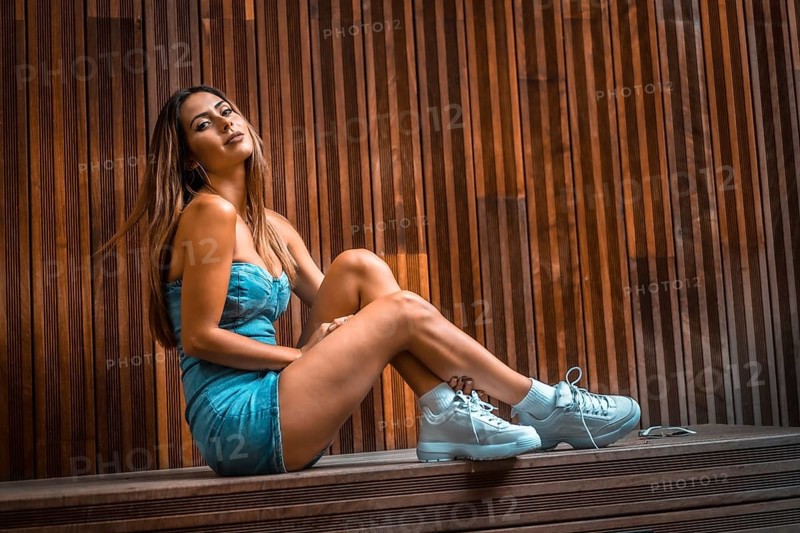 Portrait of a pretty brunette girl sitting on a wooden chair in a denim skirt