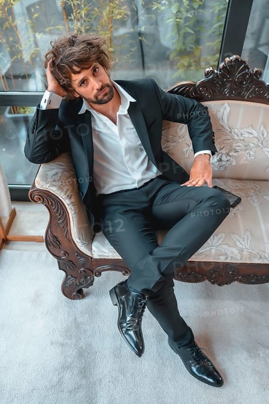 Street style with a young dark-haired caucasian man in a black suit and a white shirt in a luxurious hotel