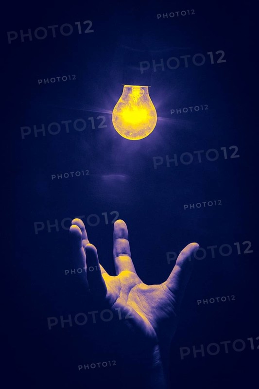 Hand reaches from below for luminous light bulb