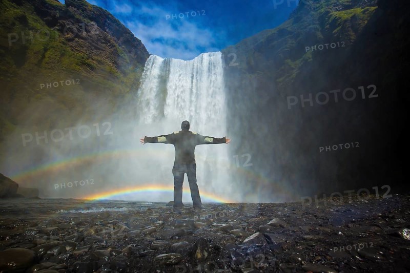 A tourist with open arms at the bottom of the Skogafoss waterfall in the golden circle
