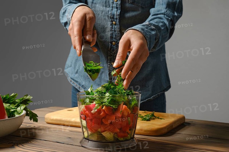 Close up view of female hands dropping chopped parsley into blender in the kitchen