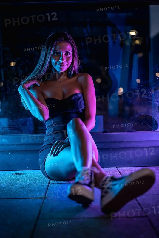 Caucasian brunette in a black dress illuminated by purple and blue led light reflected in black crystals sitting on the floor