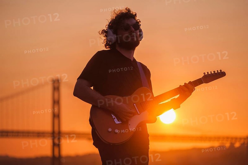 Hipster street musician in black playing electric guitar in street outdoors on sunset