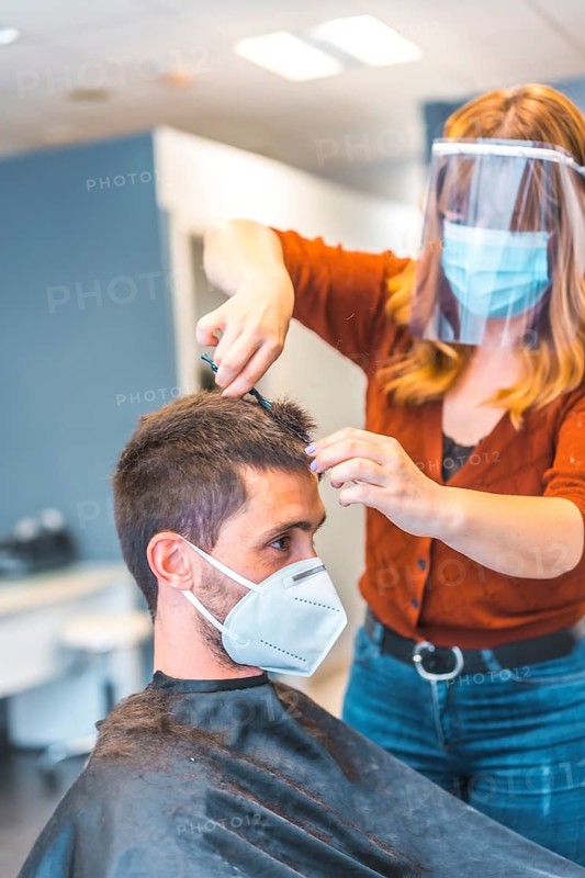 Hairdressers after the Coronavirus pandemic. Caucasian hairdresser with face mask and protective screen