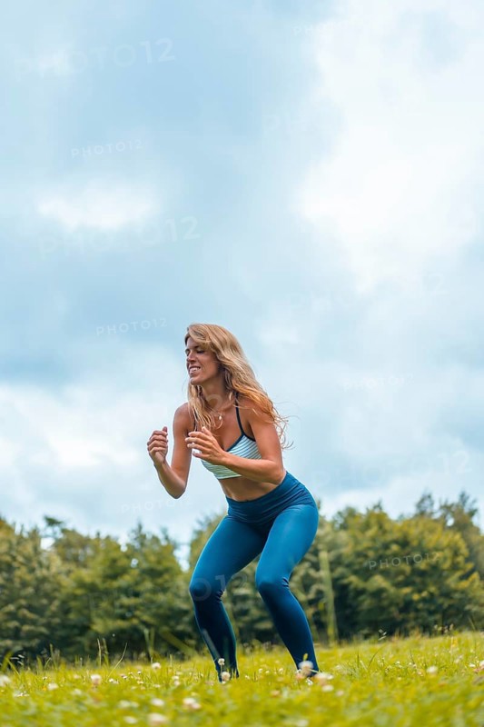 Fitness session with a young blonde caucasian woman exercising in nature with a blue maya on her feet and a white short shirt. Squatting and jumping