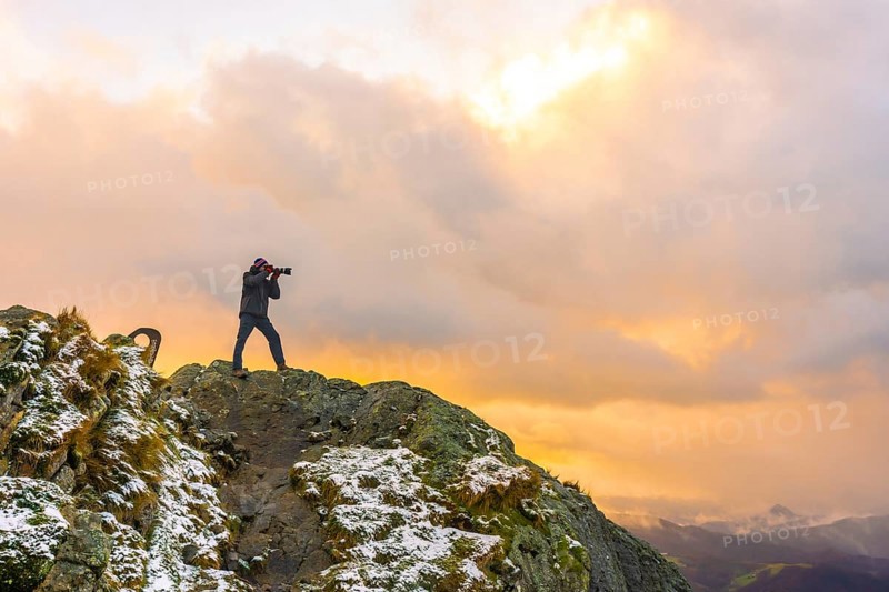A photographer on top of the mountain in the snowy winter orange sunset