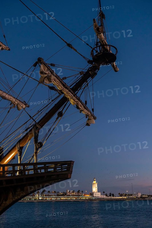 Old ship on the promenade of Muelle Uno in the Malagaport of the city of Malaga and in the background La Farola de Malaga