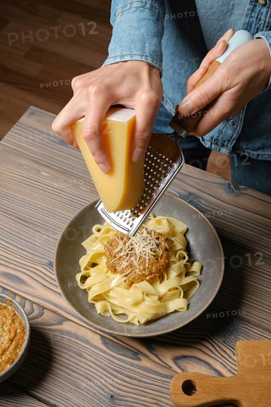 High angle view of female hands grating parmesan cheese into pasta