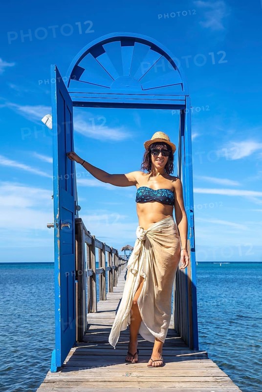A young girl at a blue door in the Caribbean Sea on Roatan Island. Honduras