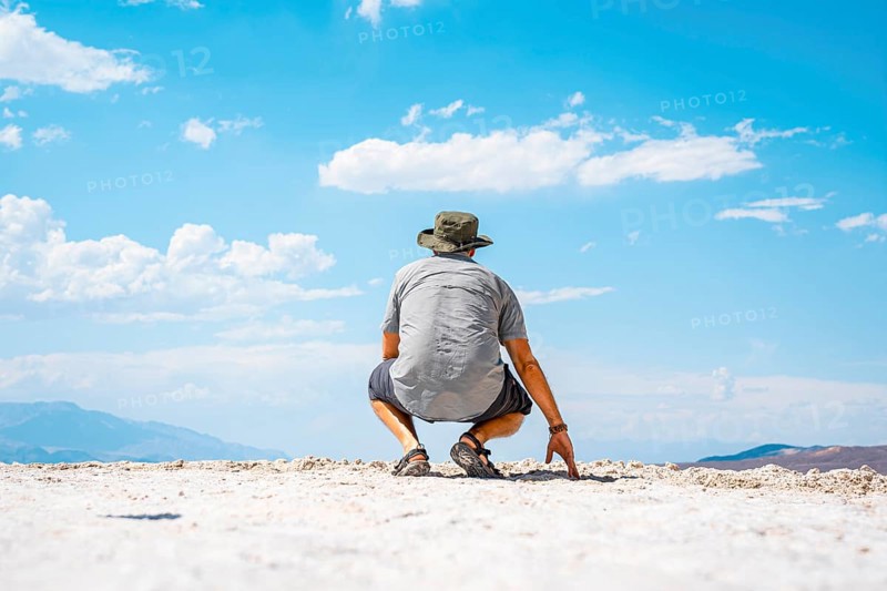 A young man crouched on his back on the white salt flat in Badwater Basin