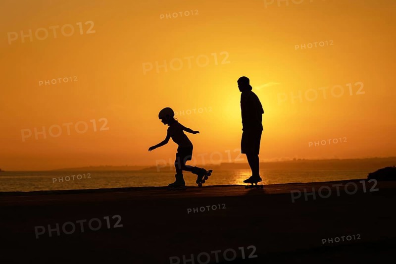 Silhouette of a man and a child skating on skateboard and roller skates. Mid shot