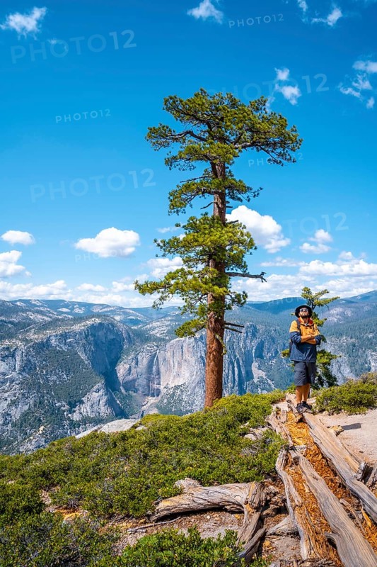 A young man with a brown jacket in Sentinel Dome looking at Upper Yosemite Fall