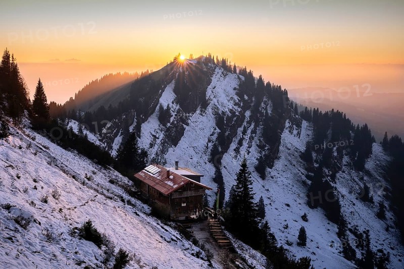 The Staufner Haus on the Hochgrat in autumn at sunset with backlight and sun star. There is snow on the slopes. Oberstaufen