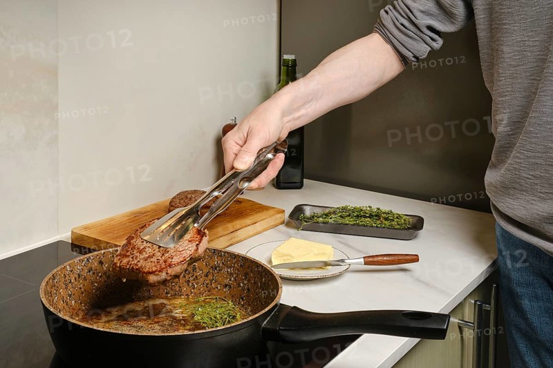 Close up view of taking out frying pan fried beefsteak with kitchen tongs