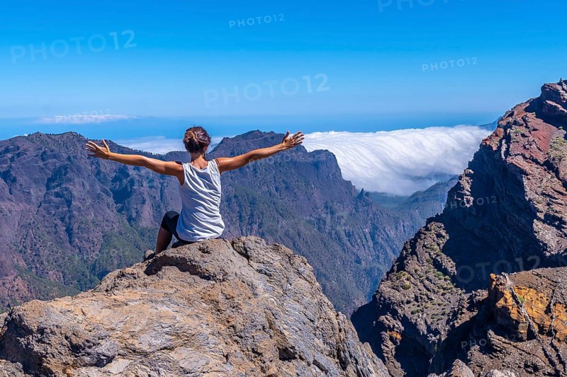 A young woman sits resting and looking at the views of the Roque de los Muchachos national park on top of the Caldera de Taburiente