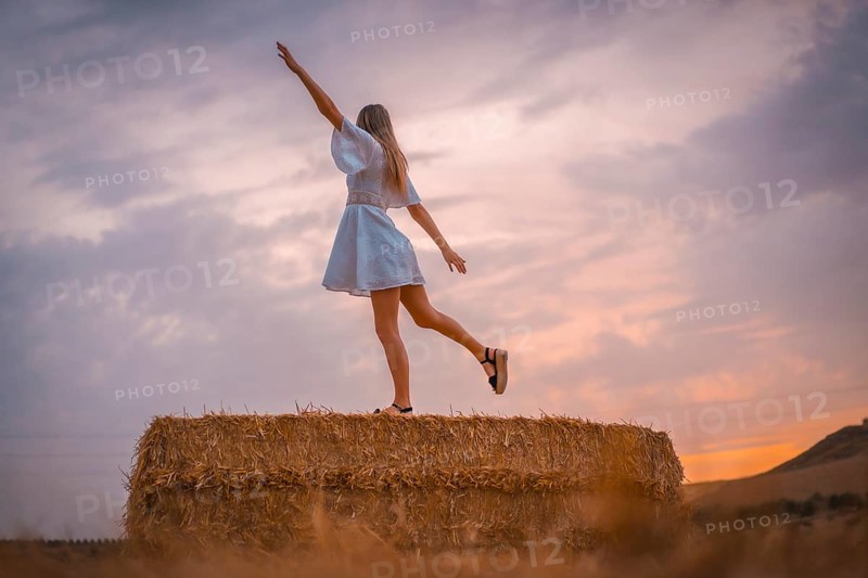 A young blonde Caucasian woman in a white dress in a field of dry straw atop a haystack. In a dry cultivated field in Navarra