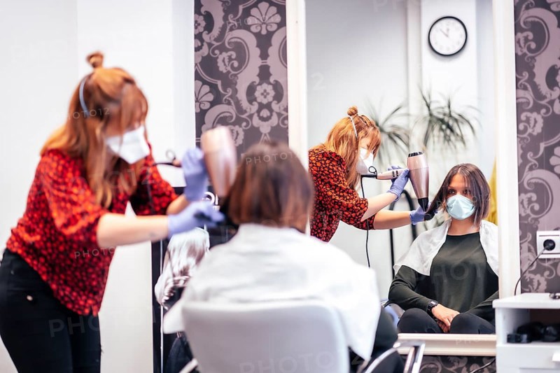 Hairdresser with mask and gloves smoothing hair of client dryer. Reopening with security measures for hairdressers in the Covid-19 pandemic