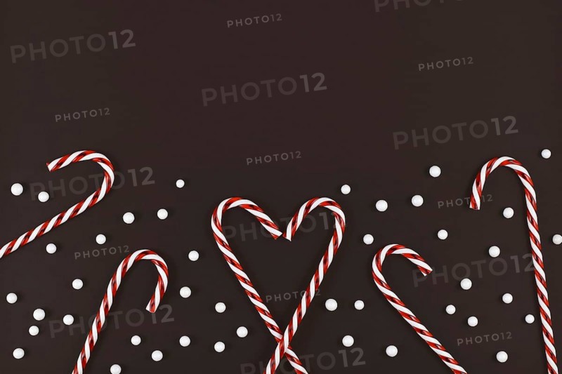 Christmas candy canes forming heart surrounded by white snowball ornaments on dark background