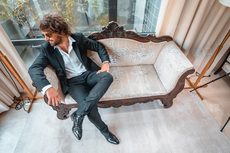 Street style with a young dark-haired caucasian man in a black suit and a white shirt in a luxurious hotel