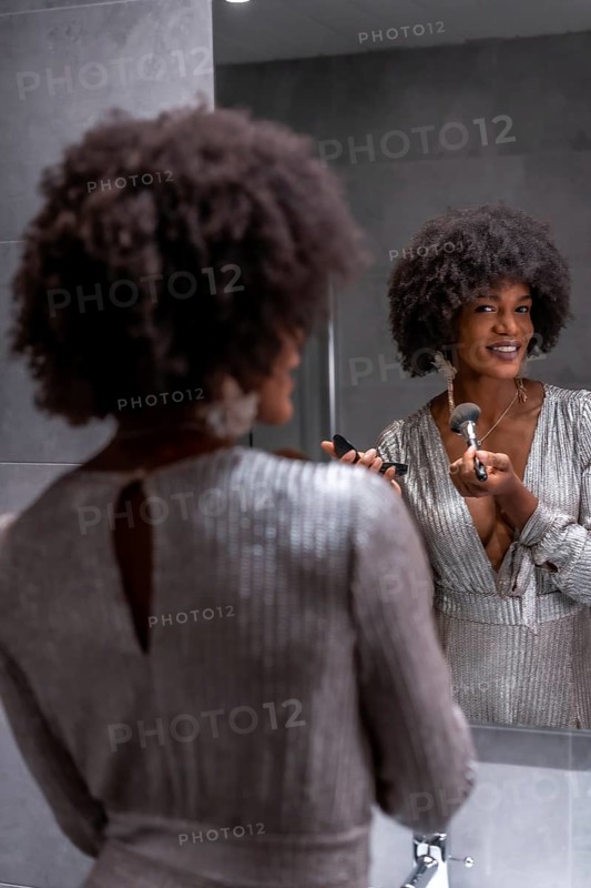 A young black girl with afro hair putting on makeup before the party with a smile. Exclusive party