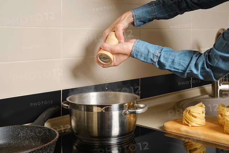 Unrecognizable woman adds salt to water boiling in saucepan on an induction stove