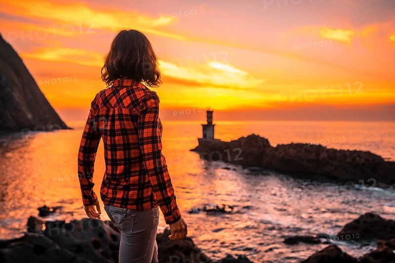 A young woman in a plaid shirt watching the sunset from the Pasajes San Juan lighthouse