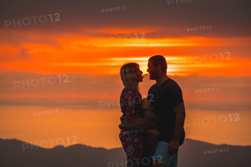 Parents on the top of a mountain at sunset and his son watching them