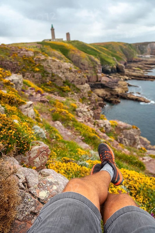 A young tourist sitting on the coast next to the Phare Du Cap Frehel